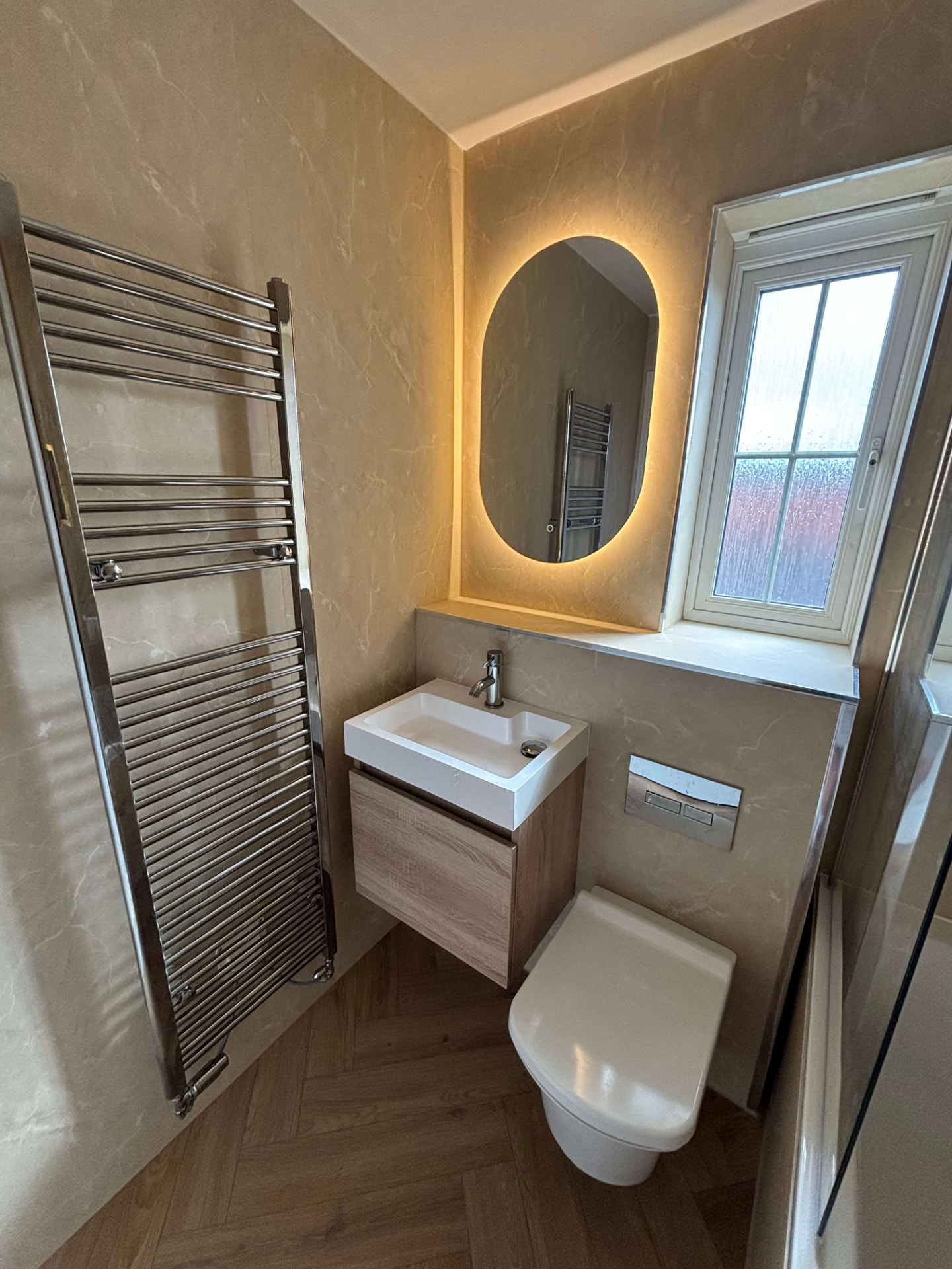 Cloakroom with chrome towel rail, backlit mirror and wall-hung vanity